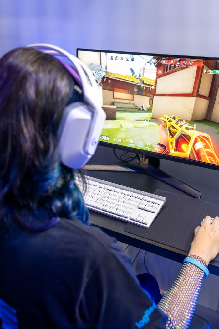 Woman immersed in gaming with headset, playing a first-person shooter on PC monitor.