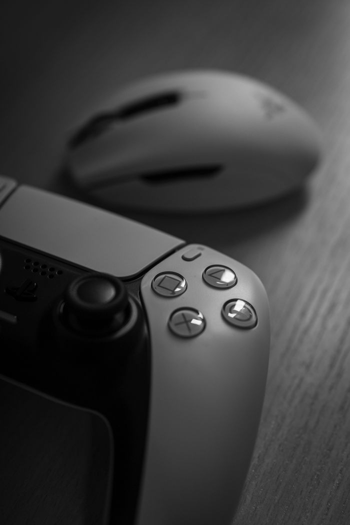 Black and white close-up of a gaming controller and mouse on a wooden surface, emphasizing buttons and ergonomic design.